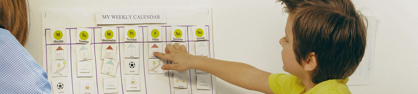 a small boy pointing to his weekly calendar.