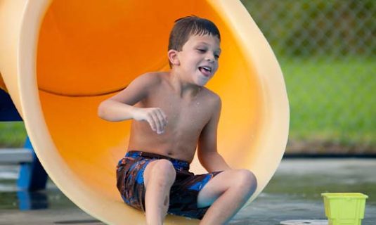 A boy sliding down a covered slide and about to make a splash into the pool at Camp Royall.