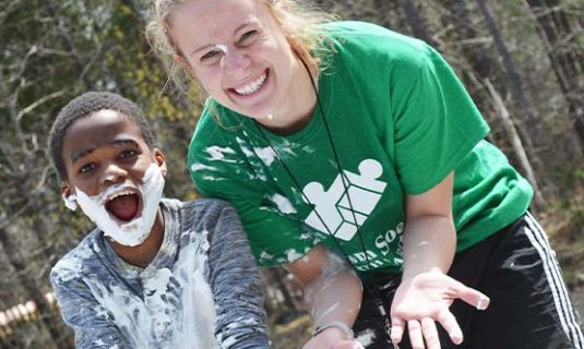 A camper and counselor having fun and making a mess with shaving cream.