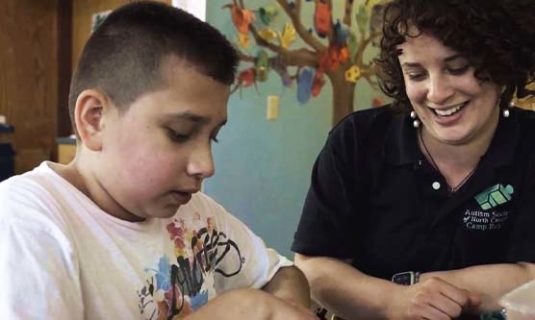 A counselor helps a camper with some crafting.