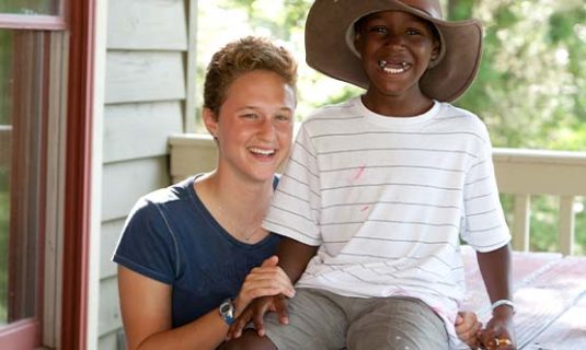 A counselor and camper smile, while the camper wears a big cowboy hat.