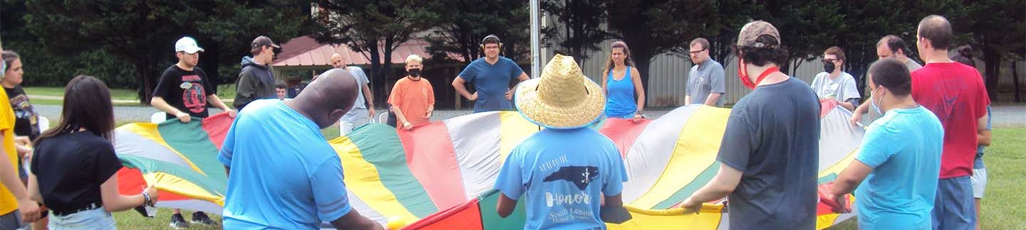 A group of campers with a large colorful parachute, doing an activity.