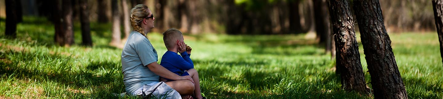 A mother and son sit together on green grass on a lovely day.