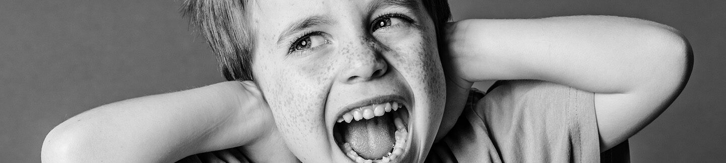 young boy holding his ears and screaming